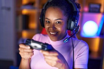 Poster - African american woman streamer playing video game using joystick at gaming room