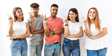 Poster - Group of young friends standing together over isolated background smiling with happy face winking at the camera doing victory sign with fingers. number two.