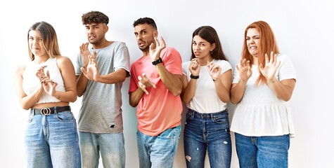 Poster - Group of young friends standing together over isolated background disgusted expression, displeased and fearful doing disgust face because aversion reaction.