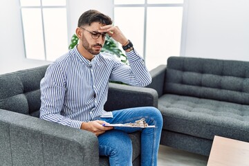 Canvas Print - Young psychologist man at consultation office worried and stressed about a problem with hand on forehead, nervous and anxious for crisis