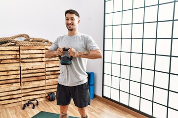 Wall Mural - Young hispanic man smiling confident training using kettlebell at sport center