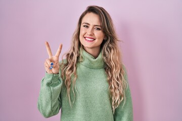 Wall Mural - Young caucasian woman standing over pink background showing and pointing up with fingers number two while smiling confident and happy.