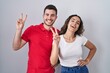© Krakenimages.com - Young hispanic couple standing over isolated background smiling looking to the camera showing fingers doing victory sign. number two.