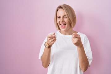 Poster - Young caucasian woman standing over pink background pointing fingers to camera with happy and funny face. good energy and vibes.