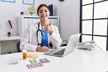 Poster - Young hispanic doctor woman wearing doctor uniform working at the clinic smiling happy and positive, thumb up doing excellent and approval sign