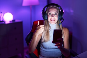 Sticker - Young caucasian woman playing video games with smartphone smiling happy and positive, thumb up doing excellent and approval sign