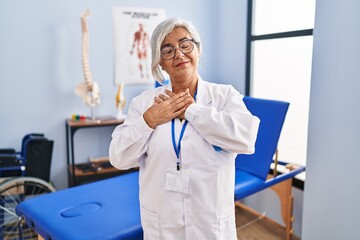 Sticker - Middle age woman with grey hair working at pain recovery clinic smiling with hands on chest with closed eyes and grateful gesture on face. health concept.