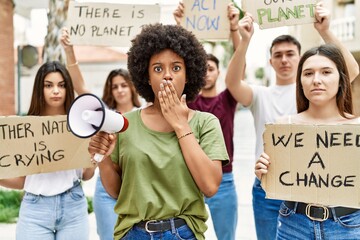 Poster - Group of young friends protesting and giving slogans at the street covering mouth with hand, shocked and afraid for mistake. surprised expression