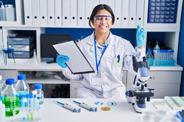 Sticker - Hispanic young woman working at scientist laboratory gesturing finger crossed smiling with hope and eyes closed. luck and superstitious concept.