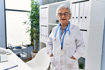 Wall Mural - Senior grey-haired woman wearing doctor uniform standing at clinic