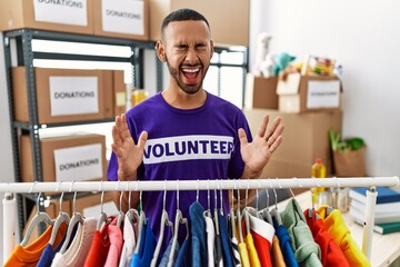 Poster - African american man wearing volunteer t shirt at donations stand celebrating mad and crazy for success with arms raised and closed eyes screaming excited. winner concept