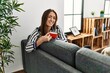 © Krakenimages.com - Young hispanic woman drinking coffee sitting on sofa at home