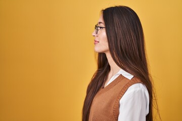 Poster - Young brunette woman standing over yellow background wearing glasses looking to side, relax profile pose with natural face with confident smile.