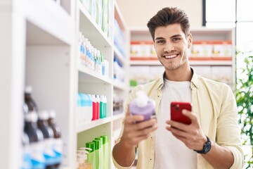 Poster - Young hispanic man customer using smartphone holding gel bottle at pharmacy