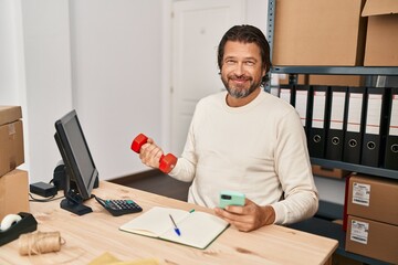 Canvas Print - Middle age man ecommerce business worker using smartphone training with dumbbell at office