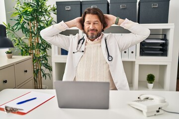 Poster - Handsome middle age doctor man working at the clinic relaxing and stretching, arms and hands behind head and neck smiling happy