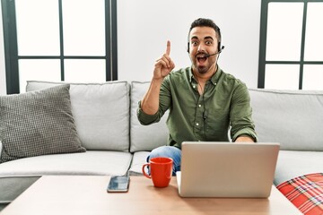 Sticker - Young hispanic man with beard wearing call center agent headset working from home pointing finger up with successful idea. exited and happy. number one.