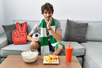 Canvas Print - Young hispanic man football hooligan cheering game at home touching mouth with hand with painful expression because of toothache or dental illness on teeth. dentist concept.