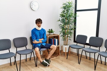 Sticker - Young hispanic man sitting at doctor waiting room with neck injury skeptic and nervous, disapproving expression on face with crossed arms. negative person.