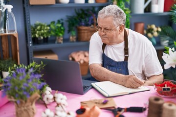 Canvas Print - Middle age grey-haired man florist writing on notebook using laptop at florist