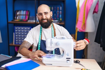 Sticker - Young bald man tailor smiling confident using sewing machine at clothing factory