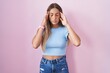 © Krakenimages.com - Young blonde woman standing over pink background with hand on head, headache because stress. suffering migraine.