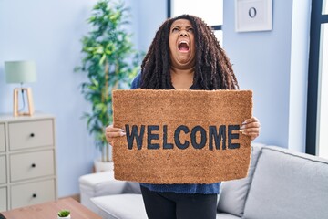 Sticker - Plus size hispanic woman holding welcome doormat angry and mad screaming frustrated and furious, shouting with anger looking up.