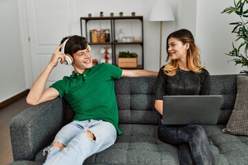 Wall Mural - Young caucasian couple smiling happy using laptop and headphones at home.