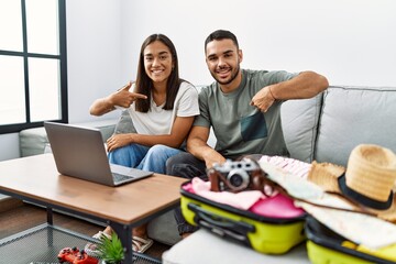 Canvas Print - Young interracial couple packing summer clothes in suitcase looking at laptop pointing finger to one self smiling happy and proud