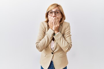 Canvas Print - Middle age blonde business woman standing over isolated background laughing and embarrassed giggle covering mouth with hands, gossip and scandal concept