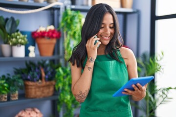 Sticker - Young hispanic woman florist talking on smartphone using touchpad at florist shop