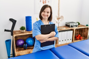 Canvas Print - Brunette woman with down syndrome working holding clipboard at physiotherapy clinic