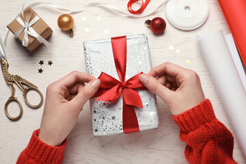 Wall Mural - Christmas present. Woman tying ribbon bow on gift box at white wooden table, top view