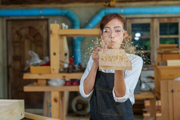 portrait of beautiful asian woman carpenter dealing with handicraft, woman has own business connected with making wooden furniture in workshop