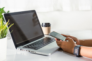 Programmer woman looking mobile phone program code at workplace, software developer hands typing data coding programming javascript with laptop computer, IT startup concept, Web application design