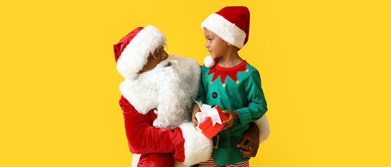 Sticker - Little African-American boy in elf costume with gift and Santa Claus on yellow background