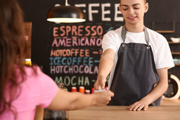 Wall Mural - Young male barista receiving payment from visitor in cafe