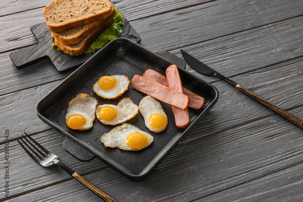 Frying pan with fried quail eggs and sausages on dark wooden background
