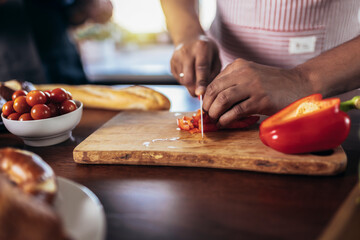 Man cooking in apron cut red pepper on wood board concept against kitchen background