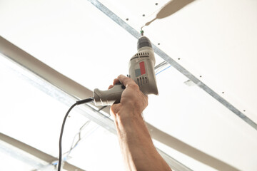 Wall Mural - Worker with a drill screwdriver twists the screw into the drywall.