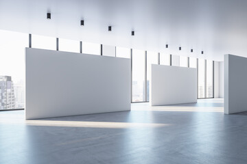 Perspective view on blank white partitions with space for advertisement or poster in sunlit empty exhibition hall with concrete floor and city view from panoramic windows. 3D rendering, mock up