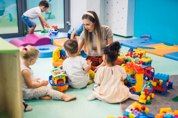 Wall Mural - preschoolers sitting on the floor surrounded plenty of toys and enjoying with their teacher, nursery. High quality photo