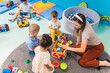 young Caucasian teacher sitting with her kids and playing with plastic toys, kindergarten and creative games concept. High quality photo