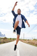© Westend61 - Man with hand raised jumping on road in front of cloudy sky
