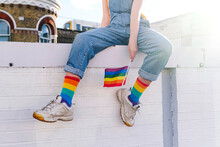 Transgender Person With Rainbow Flag Sitting On Wall