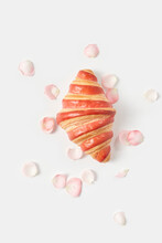 Freshly Baked Croissant Amidst Rose Petals Against White Background