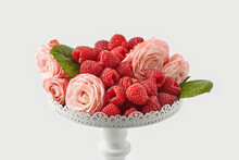 Fresh Raspberries With Pink Roses On Pedestal Cakestand Against White Background