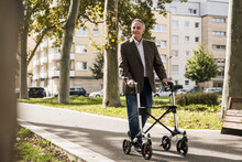 Smiling Senior Man Walking With Mobility Walker On Footpath