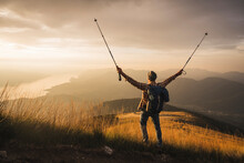 Carefree Mature Man Holding Hiking Poles Standing With Arms Raised At Sunrise