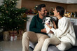 © gpointstudio - Happy couple with dog sitting at sofa in Christmas